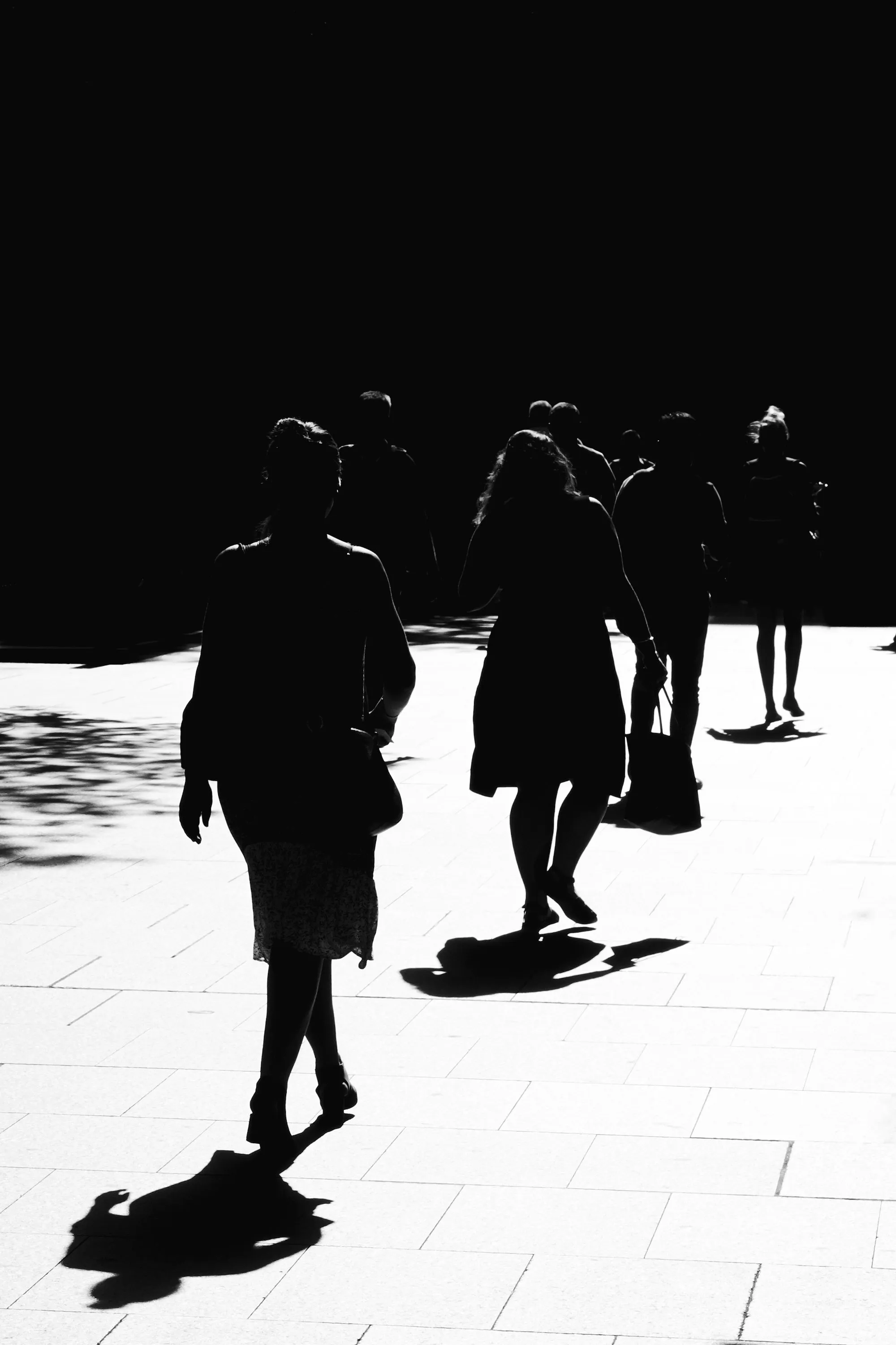 Silhouettes of people walking across a bright plaza against a dark sky